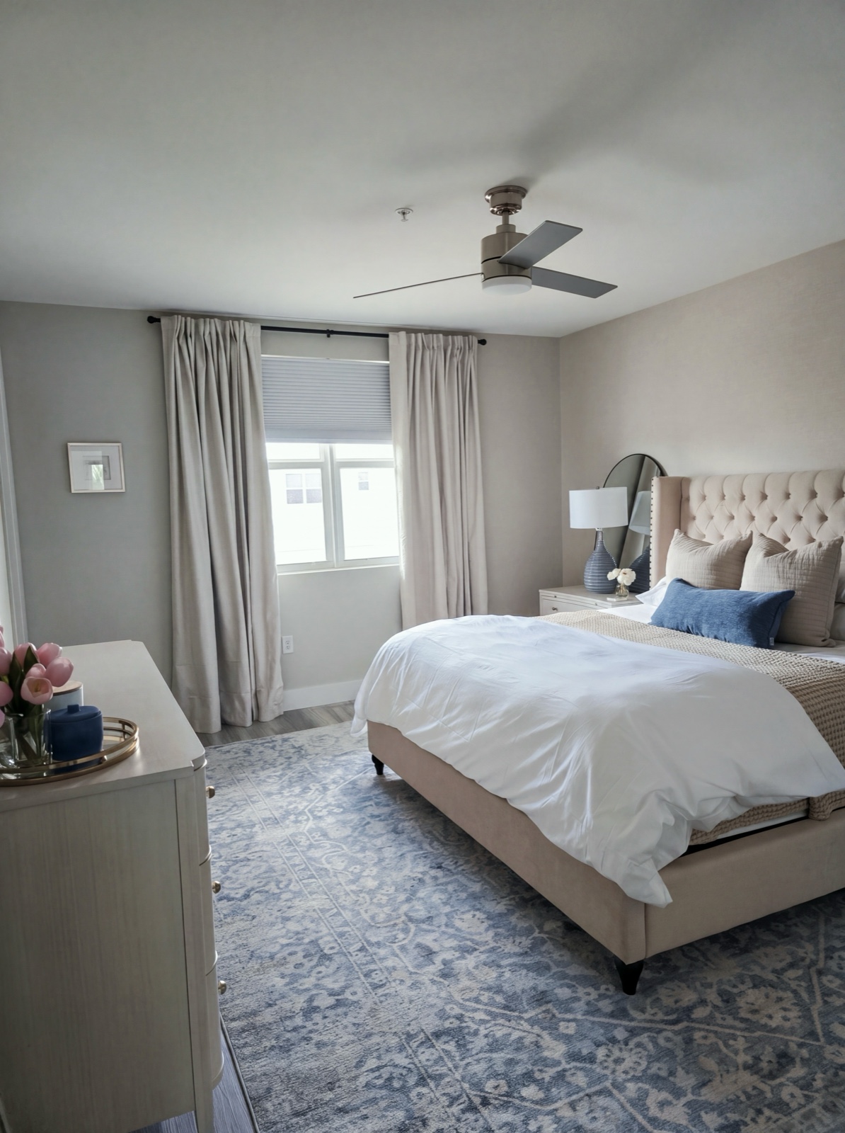 Bedroom with tufted headboard, blue medallion rug, and soft natural light