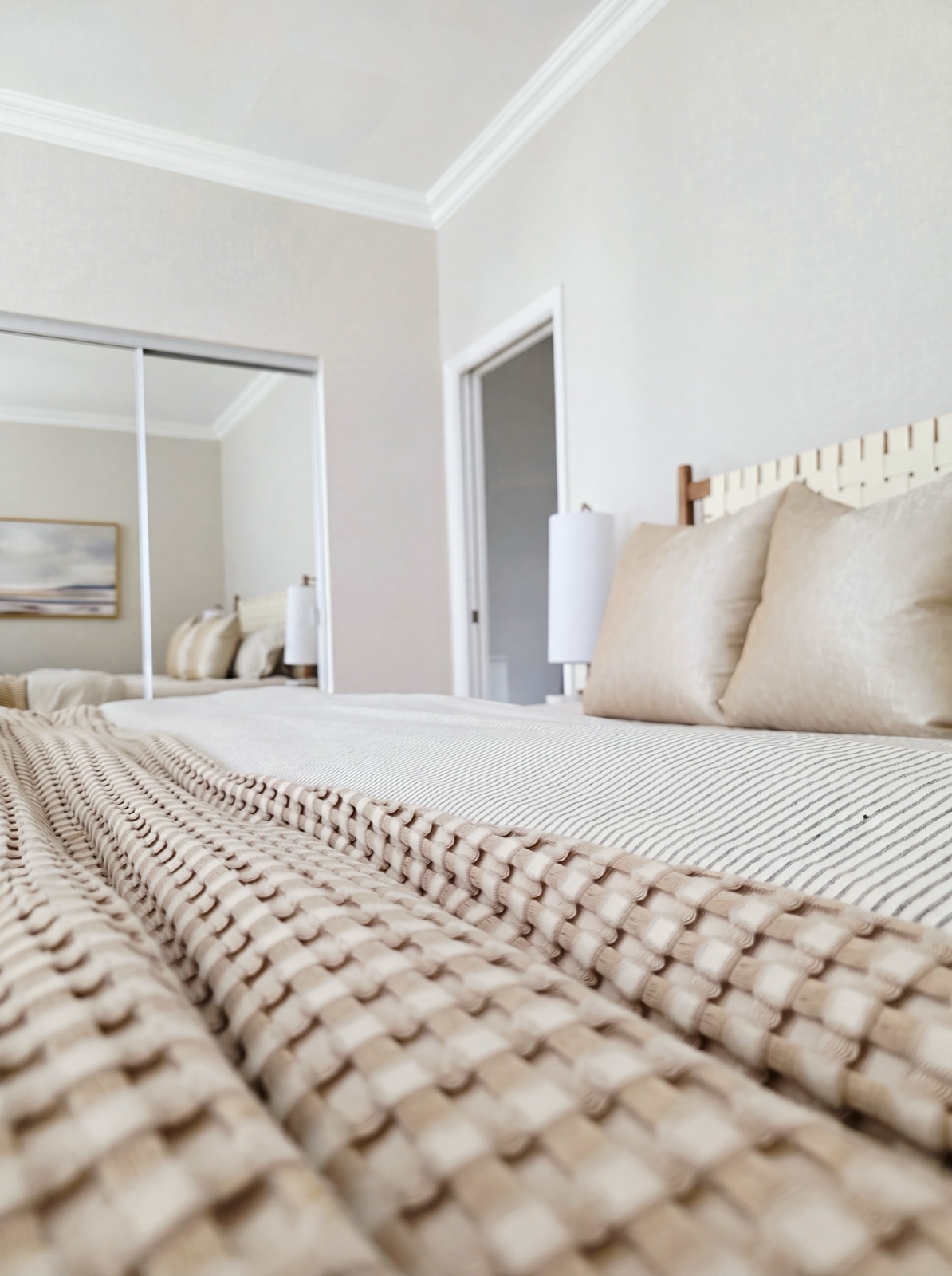 Coastal bedroom with woven headboard, waffle-knit throw, and mirrored closet