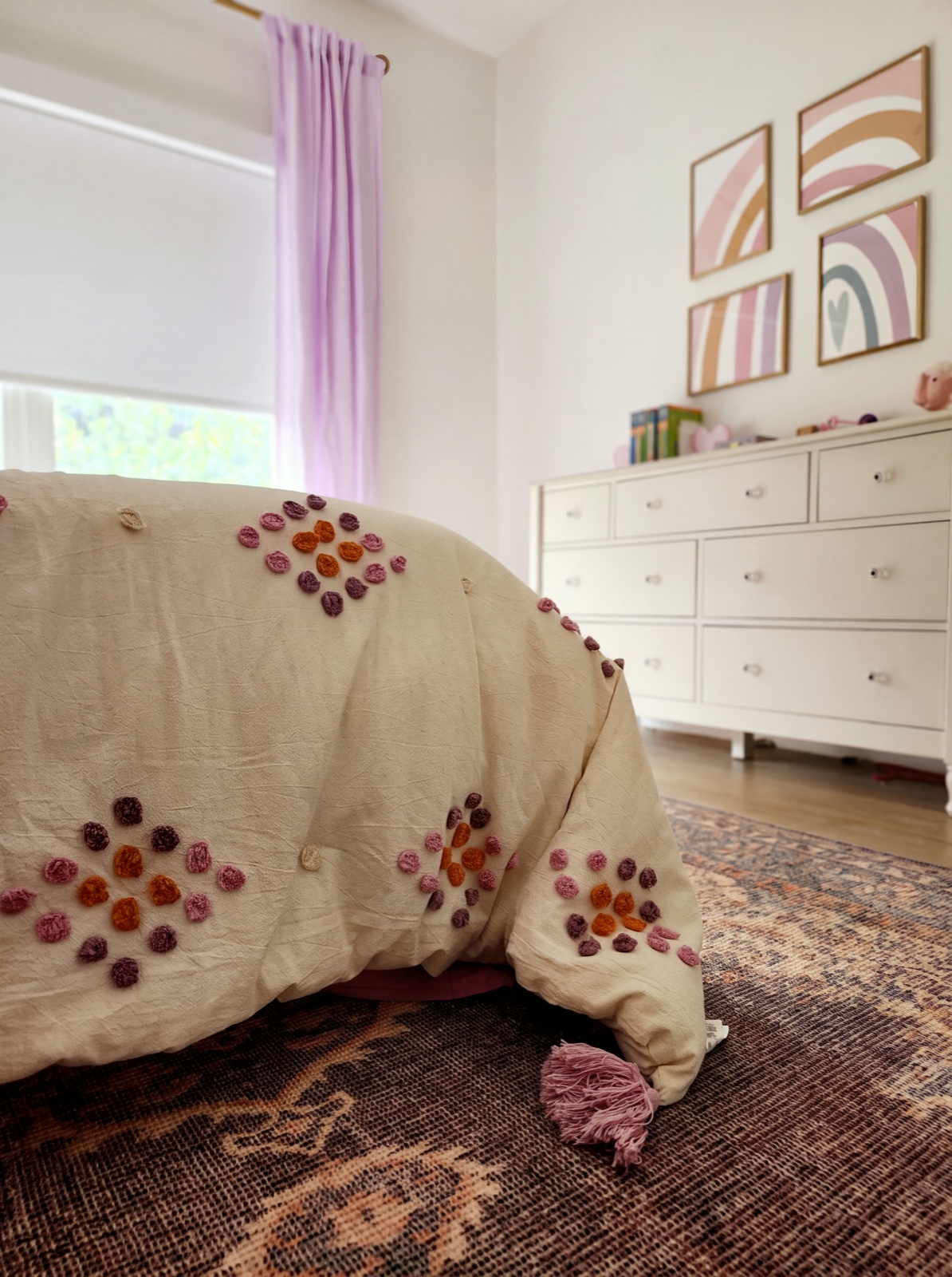 Girls' bedroom with rainbow art gallery, pom-pom duvet, and vintage rug